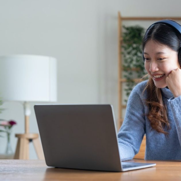 Young asian woman talk on video call at the table using headphones. Online remote work or learning